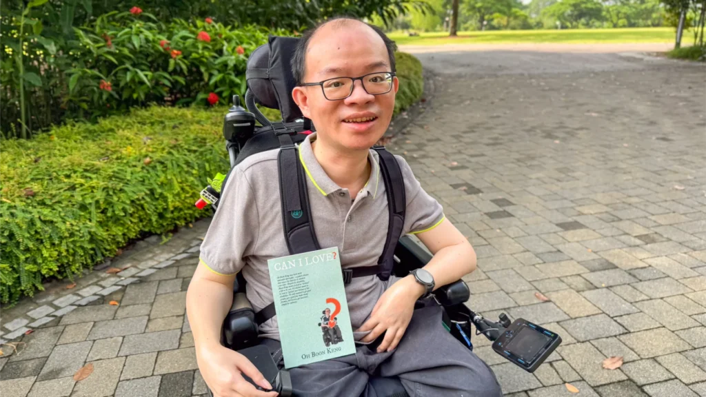 Boon Keng smiling at the camera with his book, titled ‘Can I Love?’ on his lap.