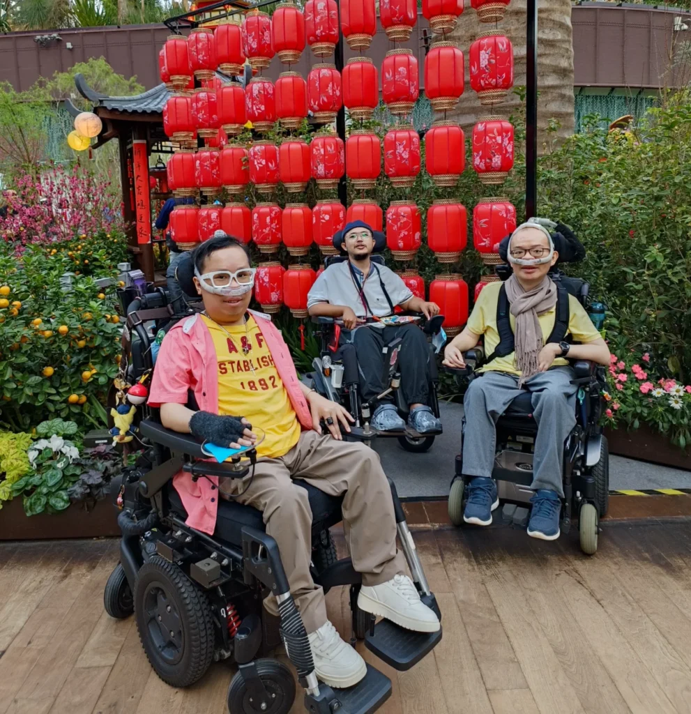 Boon Keng with two other friends at Gardens by the Bay. All of them are sitting in their electric wheelchairs, smiling at the camera.