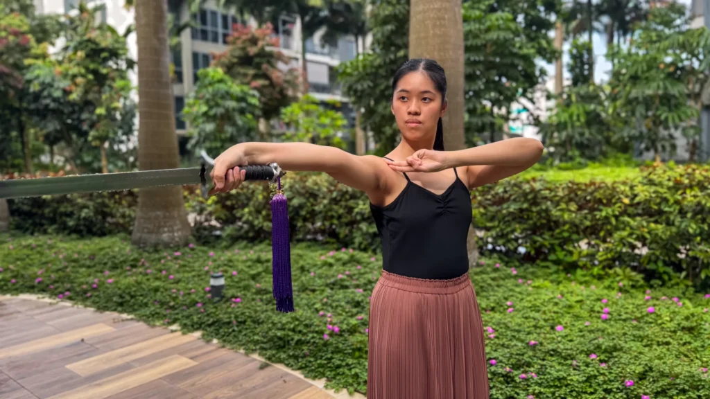 Jade stands with a serious expression in a martial arts pose, holding up her sword to face the camera.