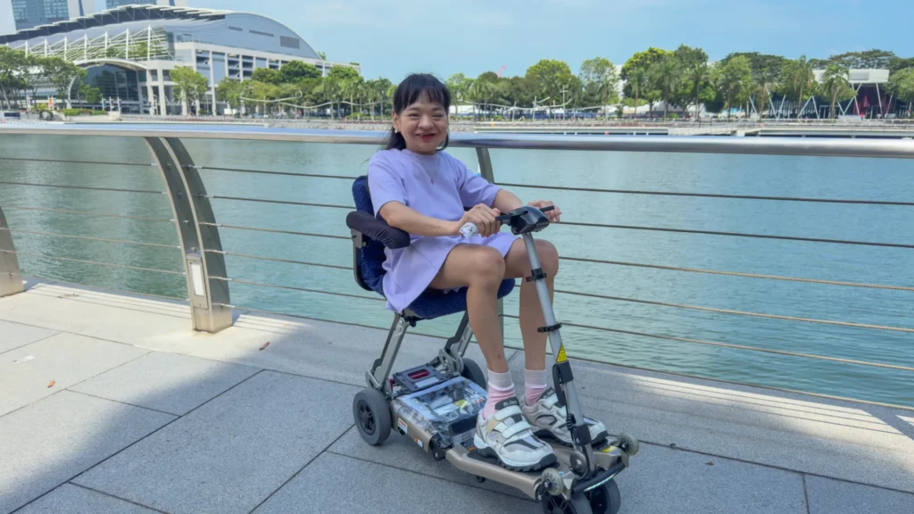 Pearl grins at the camera while sitting on her electric scooter, her hands on the handlebars. 