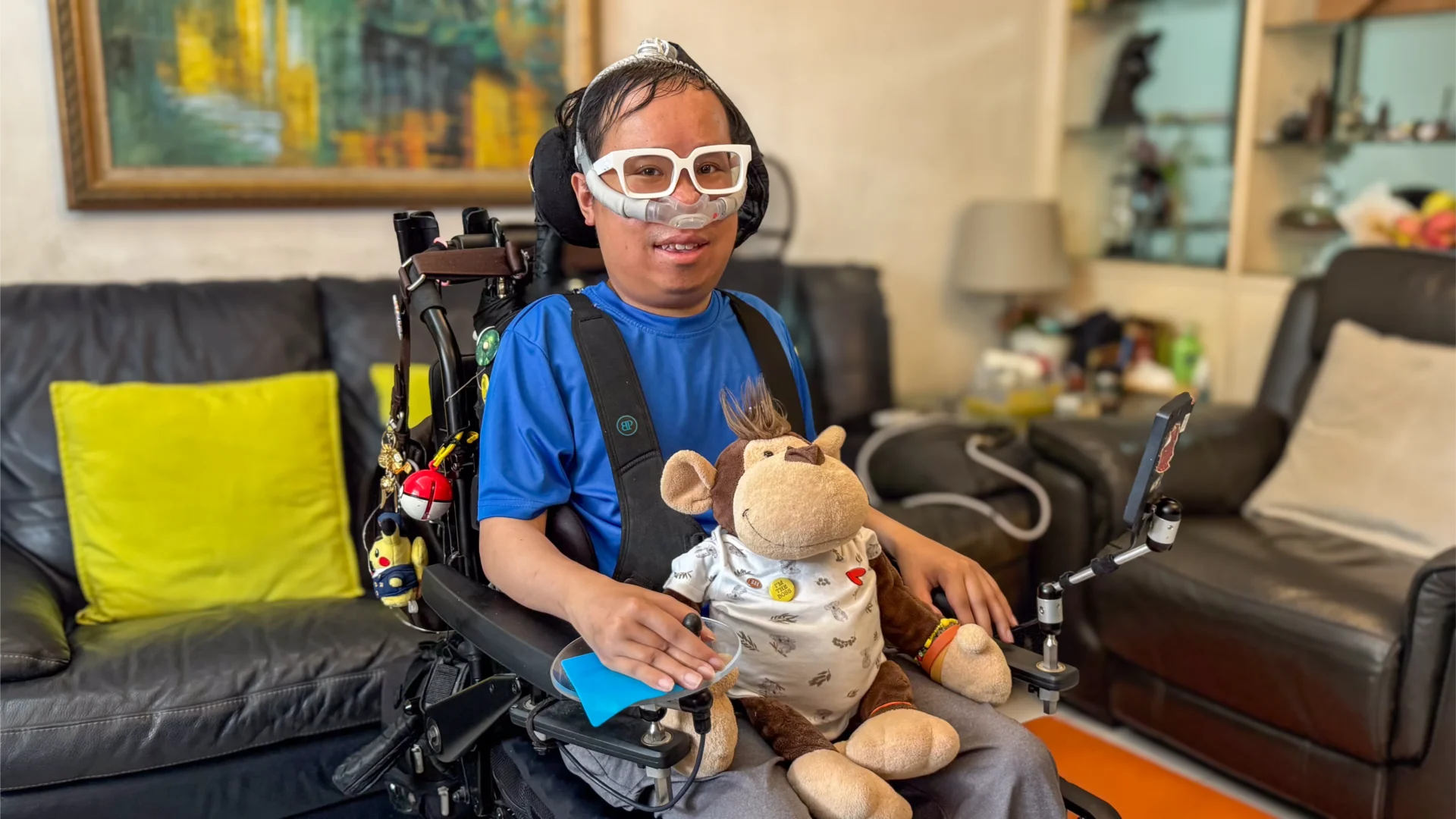 Timothy sitting in his electric wheelchair, with his stuffed toy monkey named Milford placed on his lap.