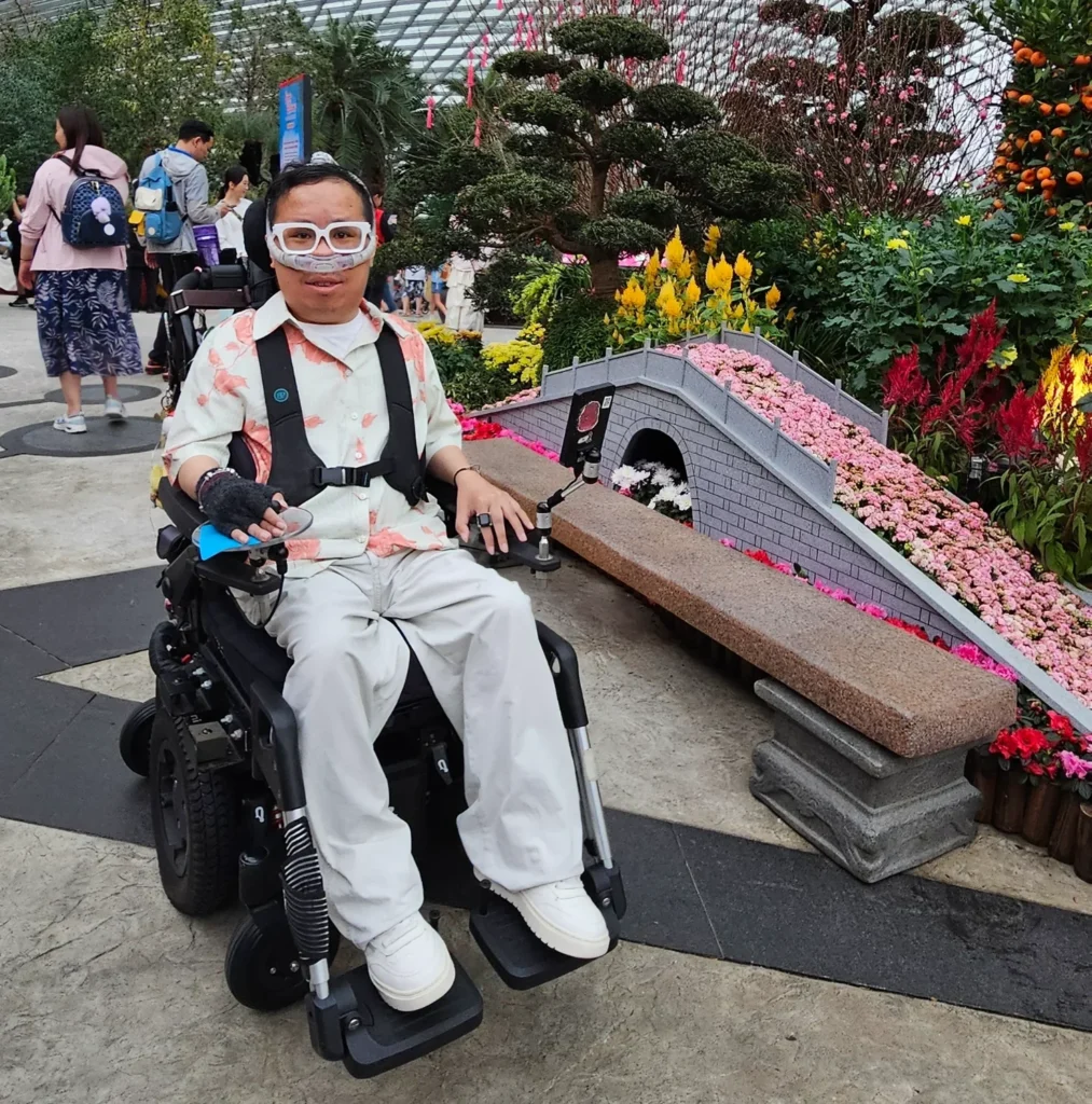 Timothy at Gardens by the Bay, dressed in a bright pink and white top which matches the bridge of pink flowers next to him.