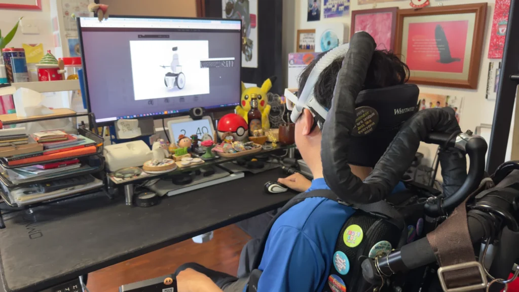 Timothy sitting at his computer, reviewing the 3D model he made of his dream wheelchair.