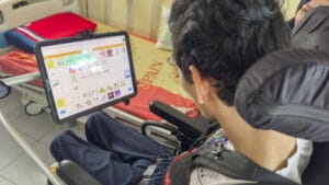 Sayfullah uses the TouchChat app on his iPad. The screen shows a message saying “I am using my AAC device to speak to you,” along with icons such as karaoke and boxing, two of his favourite hobbies.