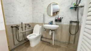 The bathroom, featuring an anti-slip grab bar by the toilet, as well as two sets of shower heads. One is installed at a normal height, and the other is installed next to the toilet for Amanda to shower while seated.