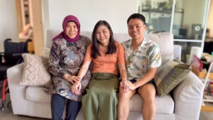 Amanda, her husband Qing Rui, and her caregiver Kakak seated on the sofa, posing for a family photo.