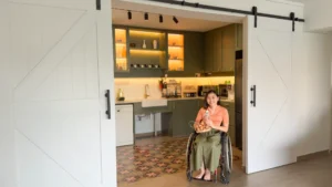 Amanda sits in her wheelchair in front of the barn doors leading into the kitchen. She is holding onto a wire chicken basket carrying eggs, nestled in her lap.