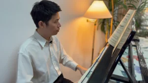 Azariah practising a piece on the grand piano, with an open book of sheet music propped against the piano.