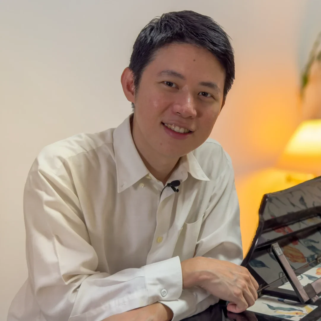 Dr Azariah Tan leaning over his grand piano, smiling at the camera.