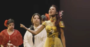Close-up shot of Claire on-stage, with an anguished expression on her face as she is speaking to the audience. She is surrounded by other cast members, who are also persons with disabilities.