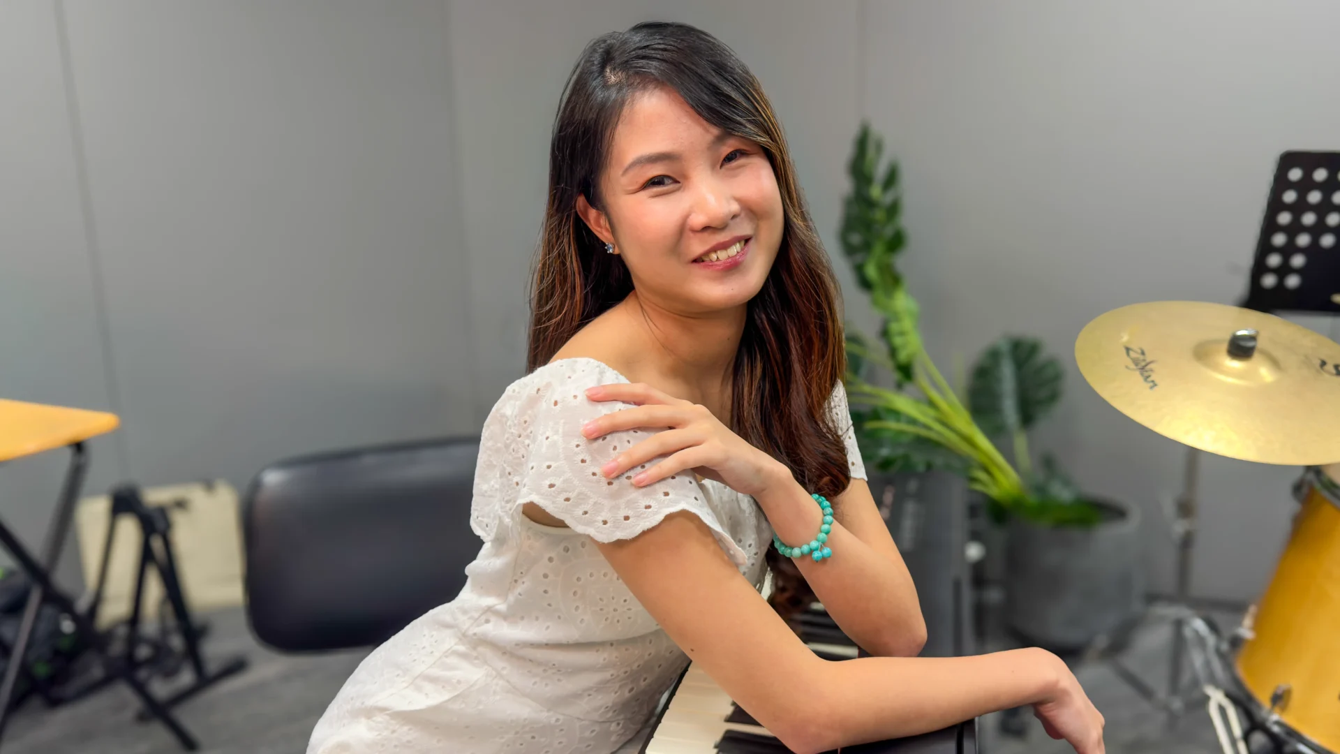 Claire Teo smiling, in a white lace dress. She is posing and leaning against a piano.