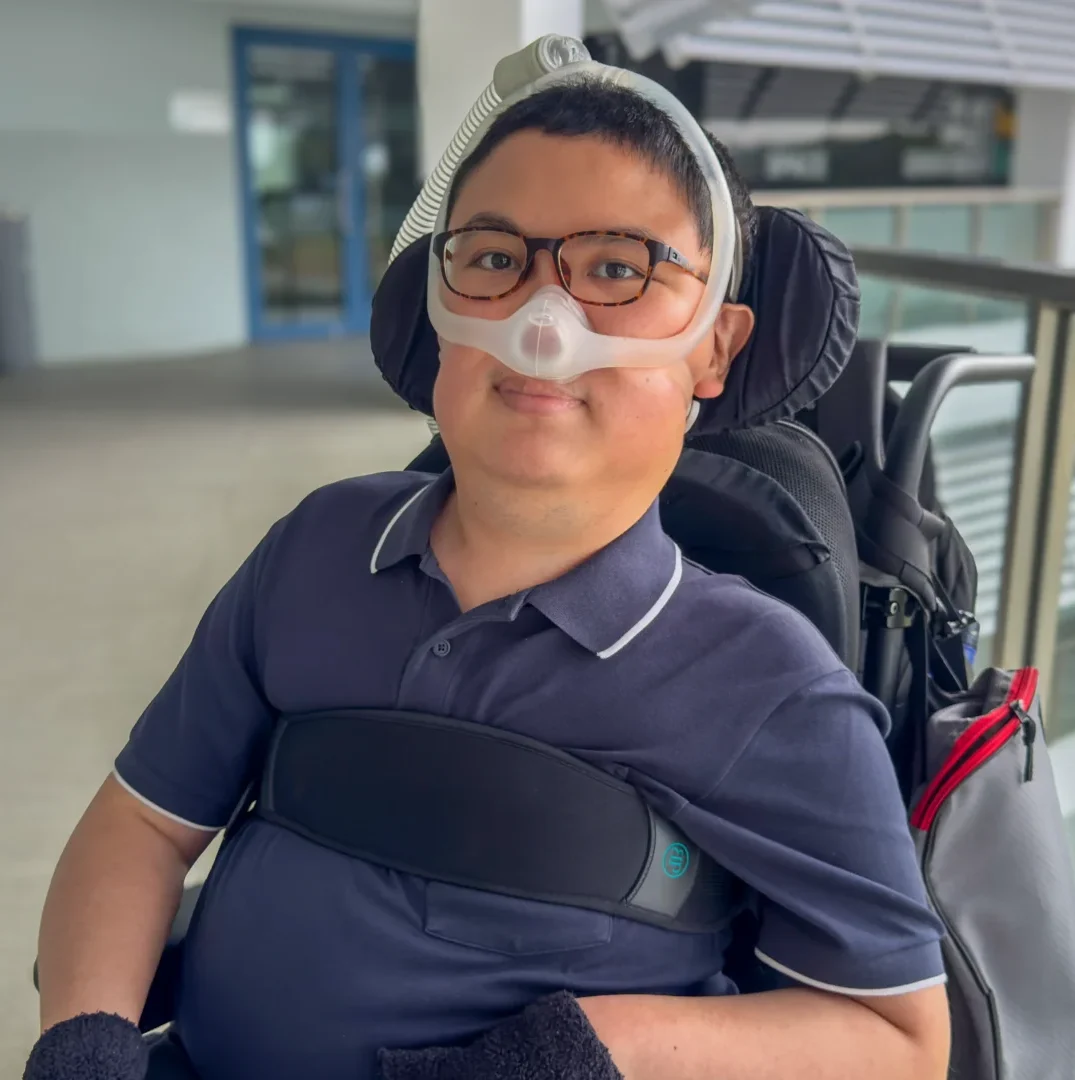 Shalom Lim, smiling at the camera and seated in his wheelchair.