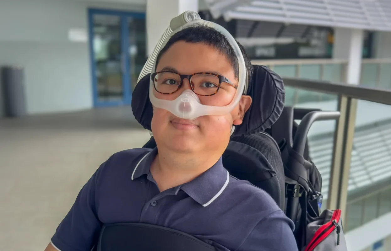 Shalom Lim, smiling at the camera and seated in his wheelchair.