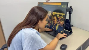 Amanda leaning towards her monitor screen, with the webpage zoomed in and tinted yellow for enhanced contrast.